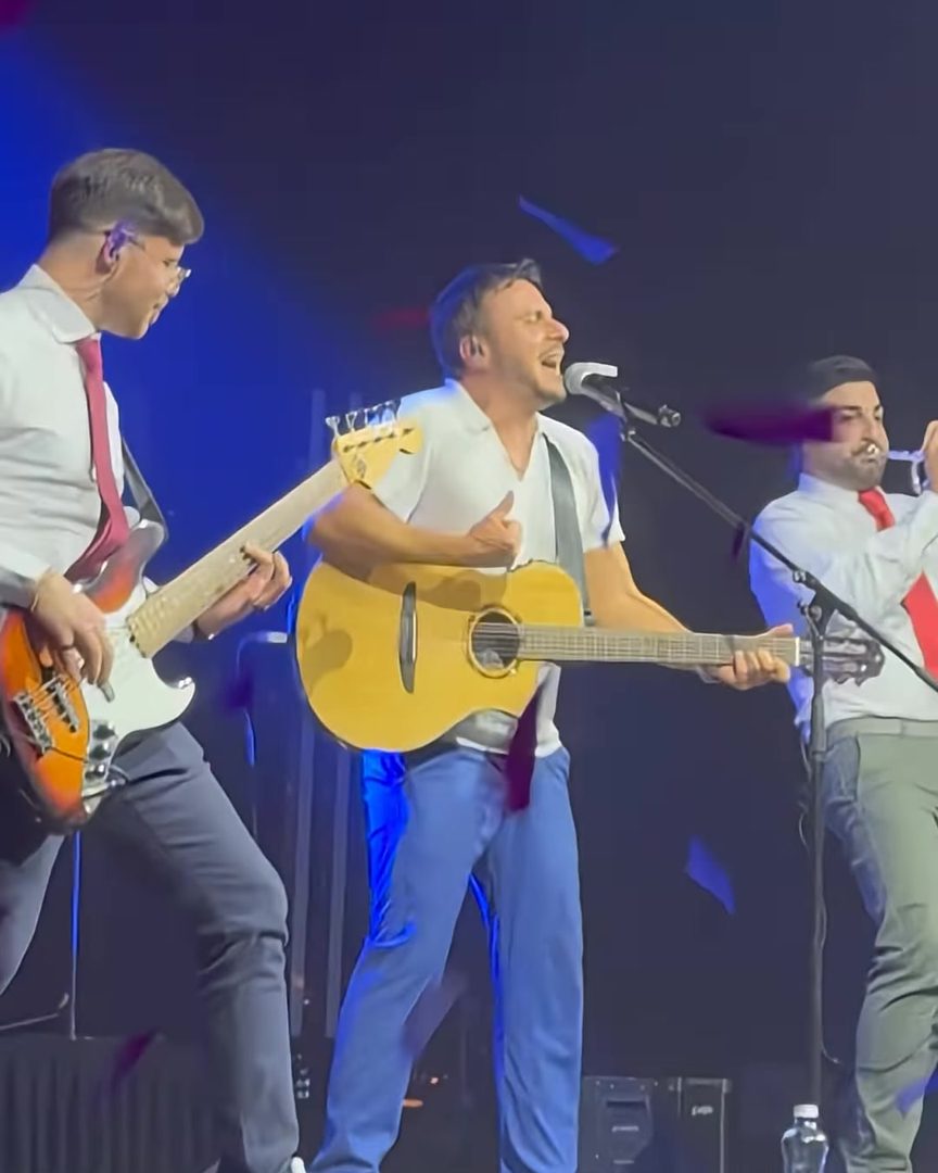 Armando Quattrone con la chitarra acustica sul palco insieme a due musicisti della band a Praga