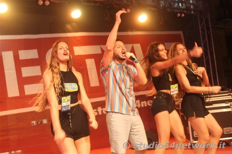 Armando Quattrone canta con il braccio alzato mentre le coriste ballano con lui sul palco